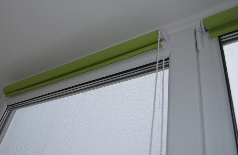 Свернутые рулонные шторы зеленого цвета на пластиковом окне